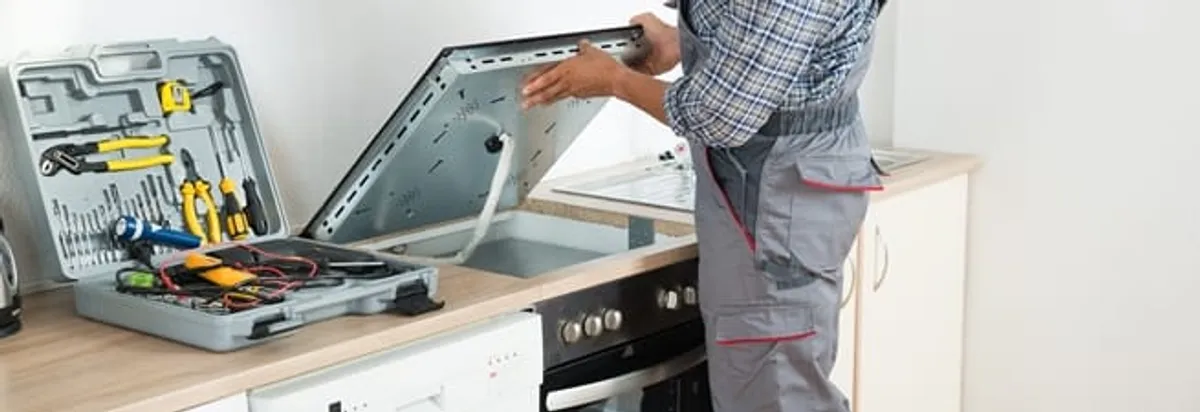 Cooktop repair technician lifting a built-in stovetop for service in Shreveport, LA